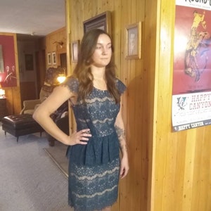 Puede incluir: Una mujer lleva un vestido de encaje azul turquesa con una cintura peplum con volantes. El vestido tiene un corpi&ntilde;o ajustado y una falda que le llega a las rodillas.
