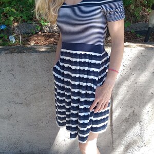 May include: A navy and white striped dress with a scoop neckline and short sleeves. The dress has a fitted bodice and a flared skirt with pockets. The skirt has a scalloped hemline. The dress is made of a soft, lightweight fabric.