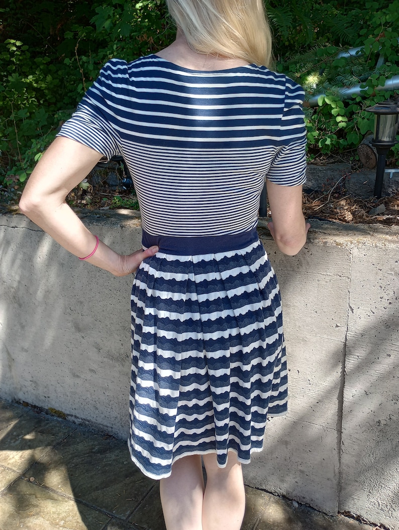 May include: A navy and white striped dress with a fitted bodice and a pleated skirt. The dress has short sleeves and a navy waistband. The skirt has a scalloped edge. The dress is knee-length.