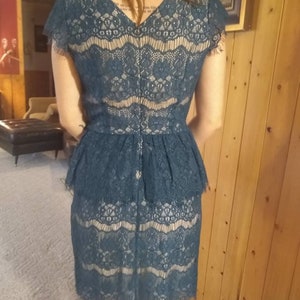 Puede incluir: Un vestido de encaje azul teal con un corpi&ntilde;o ajustado y una falda acampanada. El vestido tiene un escote en V y mangas cortas.