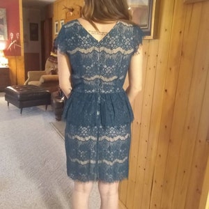 Puede incluir: Un vestido de encaje azul turquesa con un corpi&ntilde;o ajustado y una falda acampanada. El vestido tiene un escote en V y mangas cortas.