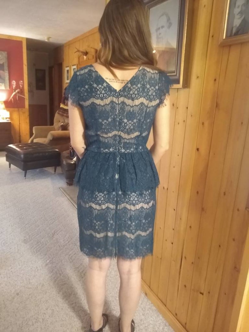 Puede incluir: Un vestido de encaje azul turquesa con un corpi&ntilde;o ajustado y una falda acampanada. El vestido tiene un escote en V y mangas cortas.