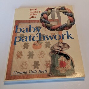 Puede incluir: Un libro titulado "baby patchwork" con un subtítulo "small quilts & other gifts" de Gianna Valli Berti. La portada presenta una colcha de retazos con diseños de ositos de peluche, una corona de retazos y una bolsa de retazos.