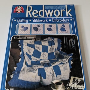 May include: A book titled "Redwork in Blue" by Laurene Sinema, featuring quilting, stitchwork, and embroidery designs. The cover shows a blue and white quilt with a butterfly design, a cup of coffee, and a signature by Suzanne Neill.