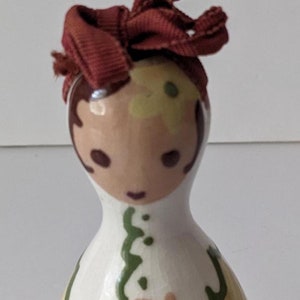 May include: A ceramic figurine of a woman with a red fabric bow on her head. She is wearing a yellow and green dress and has a painted face. The figurine is white with brown lettering that reads "DARN IT".