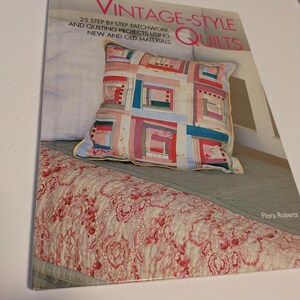 May include: A book titled "Vintage-Style Quilts" with a patchwork cushion. The cushion has a colourful design with red, pink, blue, and white squares. The book cover also displays the text "25 Step-by-Step Patchwork and Quilting Projects Using New and Old Materials."