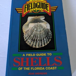 May include: A blue "Field Guide" book featuring a seashell on the cover. The book's title reads "A Field Guide to Shells of the Florida Coast" with the author's name, Jean Andrews, below.