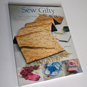 May include: A book titled "Sew Gifty" with a gold and blue table runner on the cover. The book features a variety of sewing projects, including fun accessories, décor accents, baby gifts, and other perfect presents. The book is by Janis Bullis.