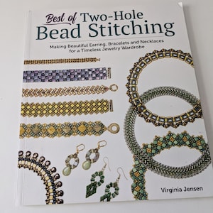 Peut inclure: Un livre intitulé "Best of Two-Hole Bead Stitching" avec un fond blanc et des motifs de bijoux en perles colorés. La couverture du livre présente une variété de colliers, de bracelets et de boucles d'oreilles en perles. Le texte "Making Beautiful Earring, Bracelets and Necklaces for a Timeless Jewelry Wardrobe" est imprimé sous le titre. Le nom de l'auteur, "Virginia Jensen", est imprimé dans le coin inférieur droit.