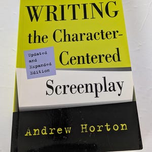 May include: A book titled "WRITING the Character-Centered Screenplay" by Andrew Horton. The cover is primarily yellow with black and white accents. A small purple sticker reads "Updated and Expanded Edition".