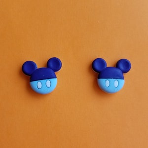May include: Two blue and light blue cartoon character shaped buttons with white eyes. The characters have large ears and a round head.