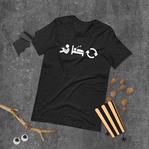 May include: Dark gray t-shirt with a white graphic depicting a person reading, sleeping, and a circular arrow. The shirt is made of a soft material and is suitable for casual wear.