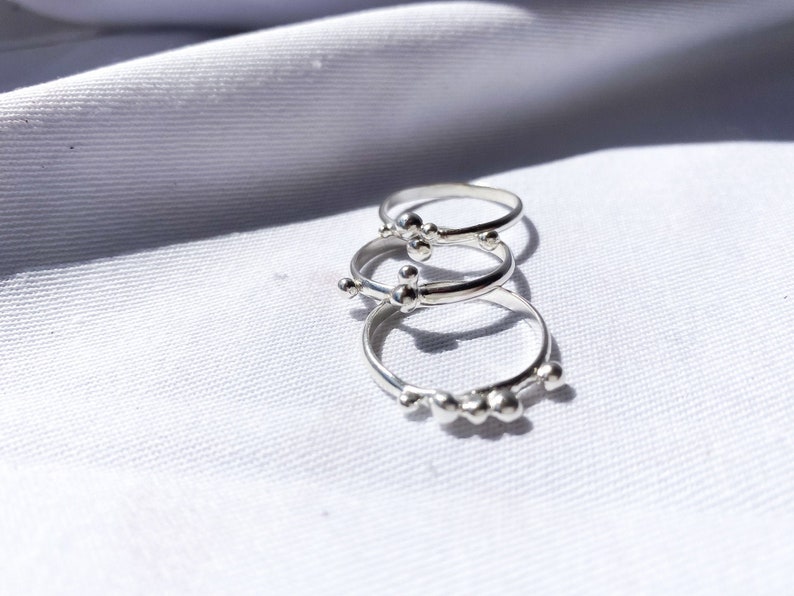 May include: Three silver rings with small, round beads. The rings are stacked on top of each other.