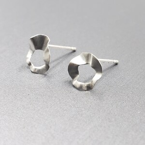 Pu&ograve; includere: Un paio di orecchini d'argento con una forma ondulata e organica. Gli orecchini hanno un piccolo foro al centro di ogni pezzo.