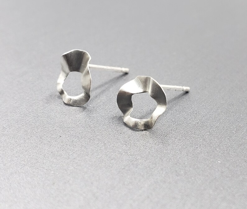 Pu&ograve; includere: Un paio di orecchini d'argento con una forma ondulata e organica. Gli orecchini hanno un piccolo foro al centro di ogni pezzo.