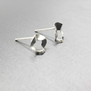 Pu&ograve; includere: Un paio di orecchini d'argento con una forma unica, organica e astratta. Gli orecchini sono realizzati in metallo sottile e hanno una superficie leggermente testurizzata.