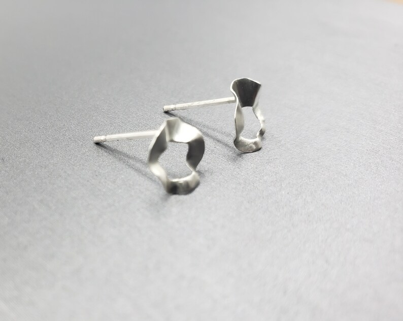 Pu&ograve; includere: Un paio di orecchini d'argento con una forma unica, organica e astratta. Gli orecchini sono realizzati in metallo sottile e hanno una superficie leggermente testurizzata.