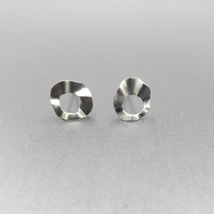 Pu&ograve; includere: Un paio di orecchini d'argento con un design circolare ondulato e testurizzato. Gli orecchini hanno un foro al centro di ogni cerchio.