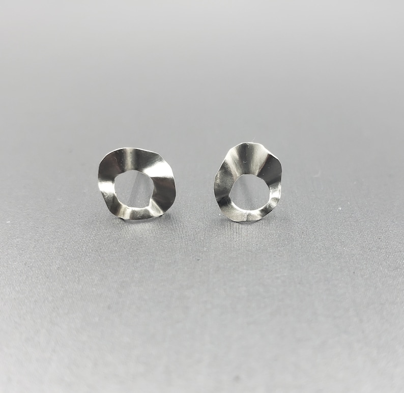 Pu&ograve; includere: Un paio di orecchini d'argento con un design circolare ondulato e testurizzato. Gli orecchini hanno un foro al centro di ogni cerchio.