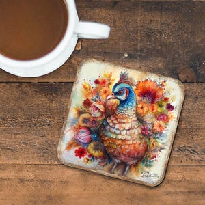 May include: A colorful coaster featuring a pheasant surrounded by flowers. The pheasant has blue, green, and brown feathers. The flowers are red, yellow, orange, and pink. The coaster has a distressed white background.