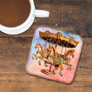 May include: Square coaster featuring a carousel design with three horses in shades of tan and cream, adorned with colorful saddles and a decorative canopy. The coaster has a watercolor effect with a pink and blue background.