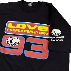 May include: Black t-shirt with a red, yellow, and blue graphic that says "LOVE PARADE BERLIN 1993" and "93". The graphic also includes a globe icon. The sleeve has a white graphic that says "love parade berlin '93".