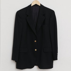 May include: A black blazer with gold buttons hangs on a wooden hanger. The blazer features a classic design with a notched lapel and two front pockets. The gold buttons are visible on the front of the blazer.