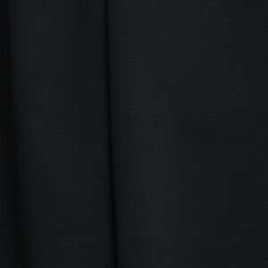 May include: Close-up of black fabric with subtle texture and folds. The image highlights the deep, solid colour and the way the material drapes, suggesting a garment or textile.