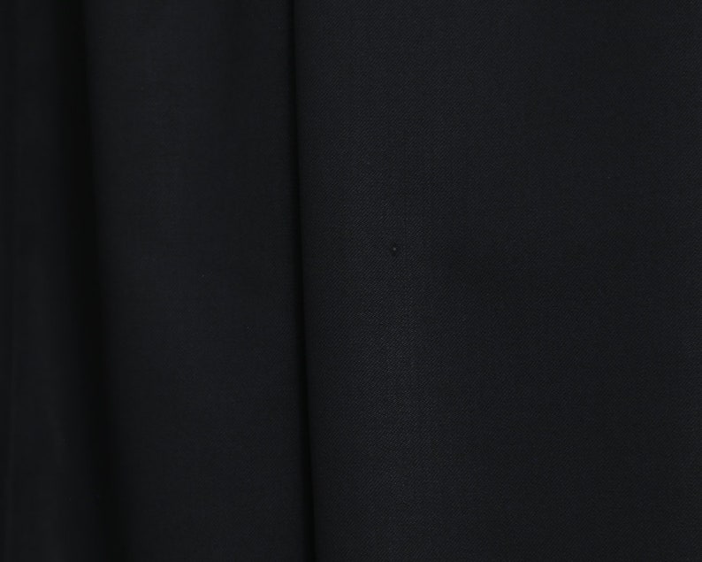 May include: Close-up of black fabric with subtle texture and folds. The image highlights the deep, solid colour and the way the material drapes, suggesting a garment or textile.