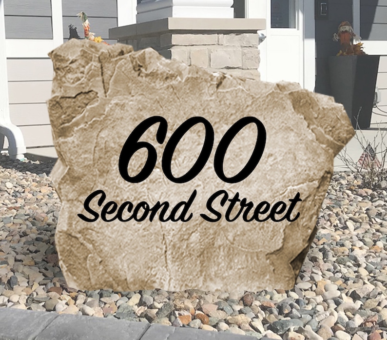 May include: A tan-colored, rock-shaped house number sign with the number 600 and the text "Second Street" in black lettering.