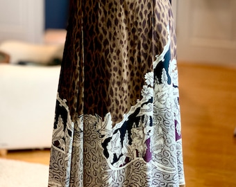 May include: A white sweater with a textured design and a brown leopard print skirt with a floral pattern at the bottom. The sweater has a brown leather belt with a silver buckle.