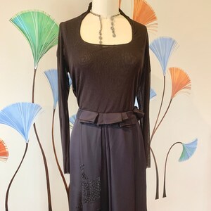 May include: A dark brown, two-piece dress with a sheer long-sleeved top and a skirt with a decorative embellishment. The dress features a square neckline and a ruffled belt. The skirt is a dark, flowing fabric.