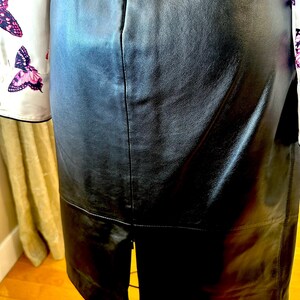 May include: A black leather skirt with a split at the back hem, displayed on a mannequin. A white blouse with butterfly patterns is partially visible on the left. The skirt is made of leather.