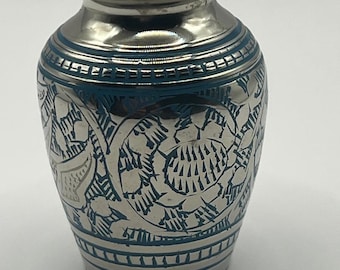 May include: Silver-toned urn with intricate floral and geometric patterns, accented with teal blue detailing. The small, decorative urn has a matching lid and is designed for keepsakes or memorial purposes.