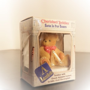 May include: A small, boxed teddy bear figurine. The bear is light brown with a red bow and a gold letter "Lambda". The box reads "Cherished Teddies Beta Is For Bears" and "Teddies with Greek Alphabet Letters in 24kt. Gold Electroplate."
