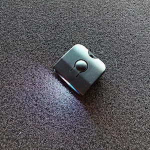 May include: A small, black, square-shaped device with a round button in the center. The device is emitting a blue light.