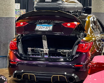 May include: A purple and gold Infiniti car with the trunk open, revealing an air suspension system. The car has a Minnesota license plate that reads "200 XPL".