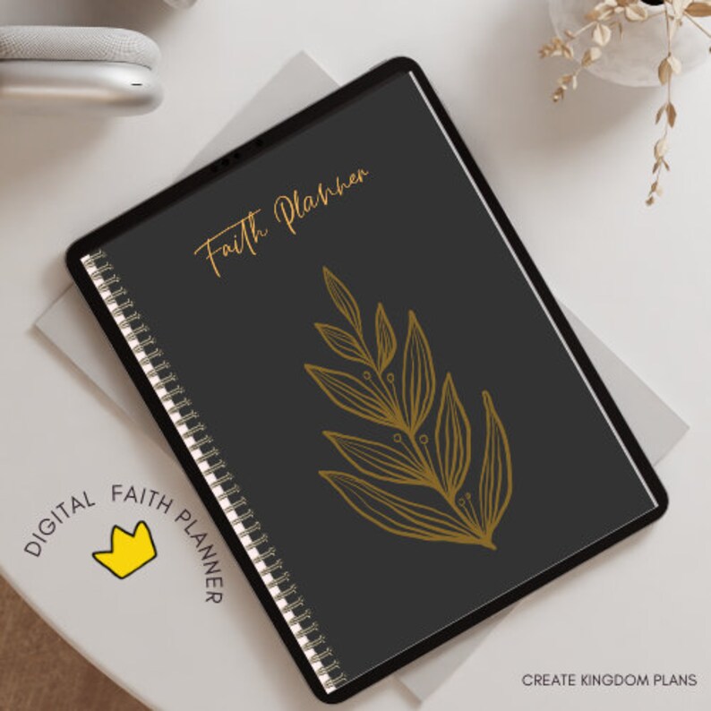 K&ouml;nnte beinhalten: Ein digitaler Planer mit schwarzem Cover und goldener Aufschrift "Faith Planner". Das Cover zeigt au&szlig;erdem ein goldenes Blattdesign. Der Planer liegt auf einer wei&szlig;en Oberfl&auml;che.