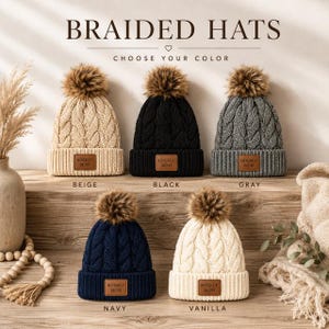 May include: Five knit beanies with cable patterns and faux fur pom-poms, arranged in two rows. Each hat features a brown rectangular patch with the text HOCKEY MOM. The colours are beige, black, grey, navy, and vanilla, labelled below each hat.