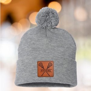 Lacrosse Mom Beanie Winter Hat Custom Leather Patch Design Cable Knit Construction Warm Winter Accessory Fur Pom Detail Sports Team Support Gear Player Name Number Personalization Cold Weather Essential Gray Knit Material Rink Side Comfort
