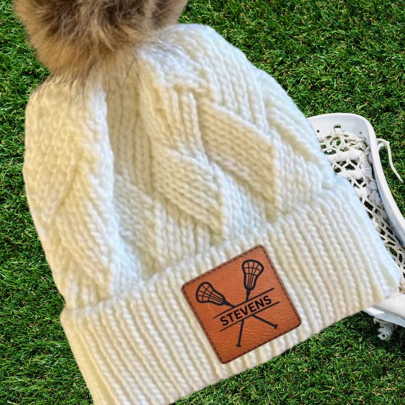 Lacrosse Mom Beanie Winter Hat Custom Leather Patch Design Cable Knit Construction Warm Winter Accessory Fur Pom Detail Sports Team Support Gear Player Name Number Personalization Cold Weather Essential Gray Knit Material Rink Side Comfort