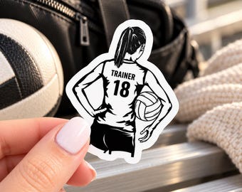 May include: A die-cut sticker featuring a black and white illustration of a person from the back, wearing a jersey with the text TRAINER and the number 18, holding a volleyball under one arm with hands on hips.