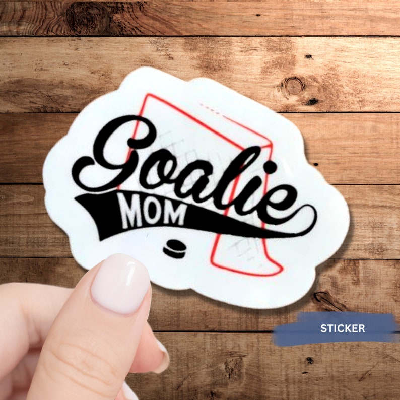 May include: White sticker with a black and red hockey net and the text "Goalie Mom" in black script font. The sticker is on a wooden background.
