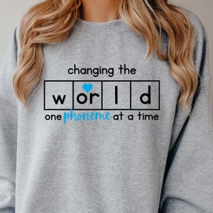 May include: Gray sweatshirt with the text "changing the world one phoneme at a time" with the word "world" in individual boxes and a blue heart in the "o" box.