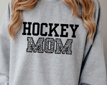 May include: Gray sweatshirt with the text "HOCKEY MOM" in black letters. The word "MOM" is outlined with a leopard print pattern.