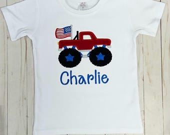 May include: White t-shirt with a red monster truck with an American flag on the back. The truck has blue star wheels and the name "Charlie" is embroidered below the truck.