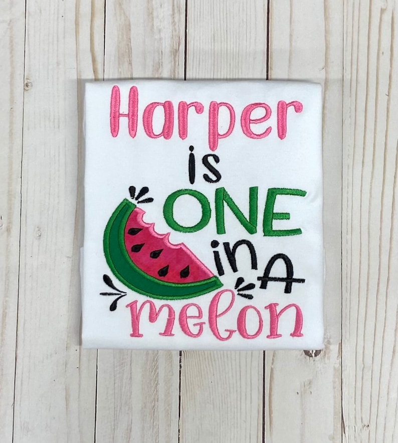 Op de afbeelding: Witte romper met roze en groene borduurwerk met de tekst "Harper is one in a melon" met een watermeloenafbeelding.