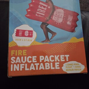 May include: A Taco Bell Fire Sauce Packet inflatable pool float. The red float is shaped like a sauce packet and features the text "FIRE!" and "I'M MY FAVORITE 100". The packaging shows a person holding the float. Dimensions are 30 inches x 57.8 inches.