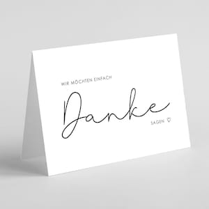 Könnte beinhalten: Eine weiße Klappkarte mit dem Wort "Danke" in eleganter schwarzer Schrift. Der Text "WIR MÖCHTEN EINFACH" steht darüber, und "SAGEN" mit einem Herzsymbol darunter. Die Karte ist innen leer, passend für verschiedene Anlässe.