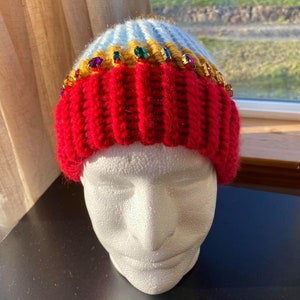 May include: A red knit beanie with a blue and yellow striped brim. The beanie is decorated with colorful rhinestones.